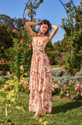 Woman in a floral dress standing in a garden with greenery and flowers around her.