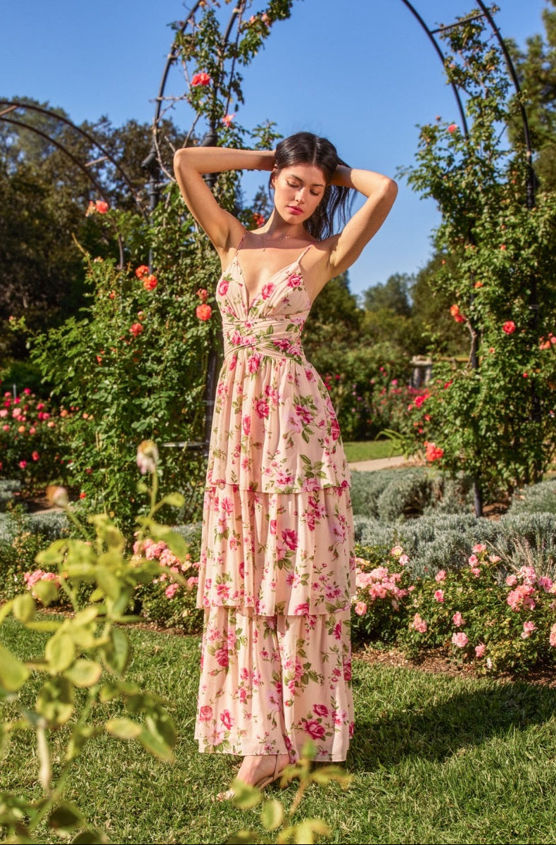 Woman in a floral dress standing in a garden with greenery and flowers around her.