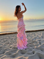 Woman in a pink floral dress standing on a beach at sunset.