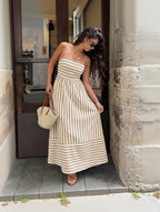 Woman in a striped dress standing against a stone wall.