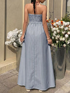Woman in a strapless blue and white striped dress standing near potted flowers.