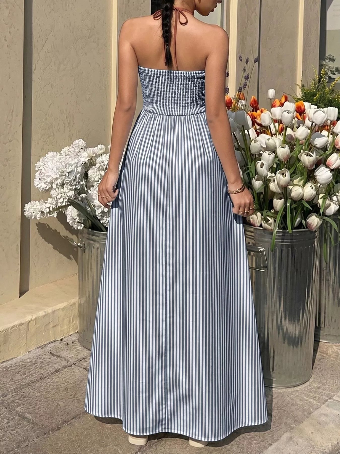 Woman in a strapless blue and white striped dress standing near potted flowers.