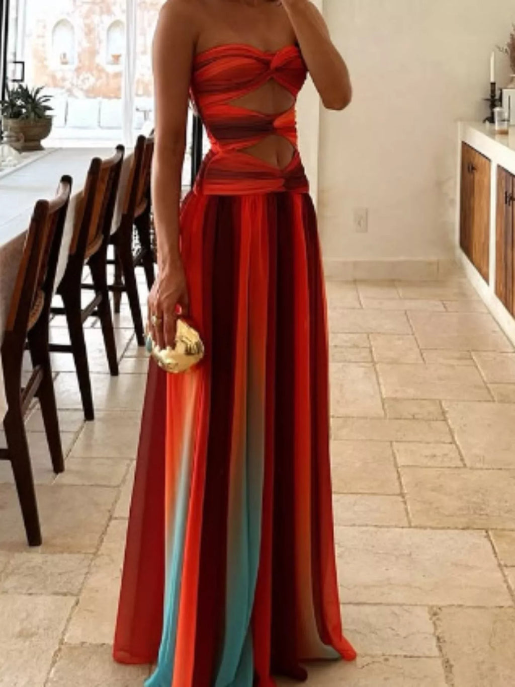 Woman wearing a red strapless dress with a long train in a room with wooden chairs and a table.