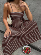 Woman in a brown and white striped dress sitting on a stone surface with a bowl of strawberries.