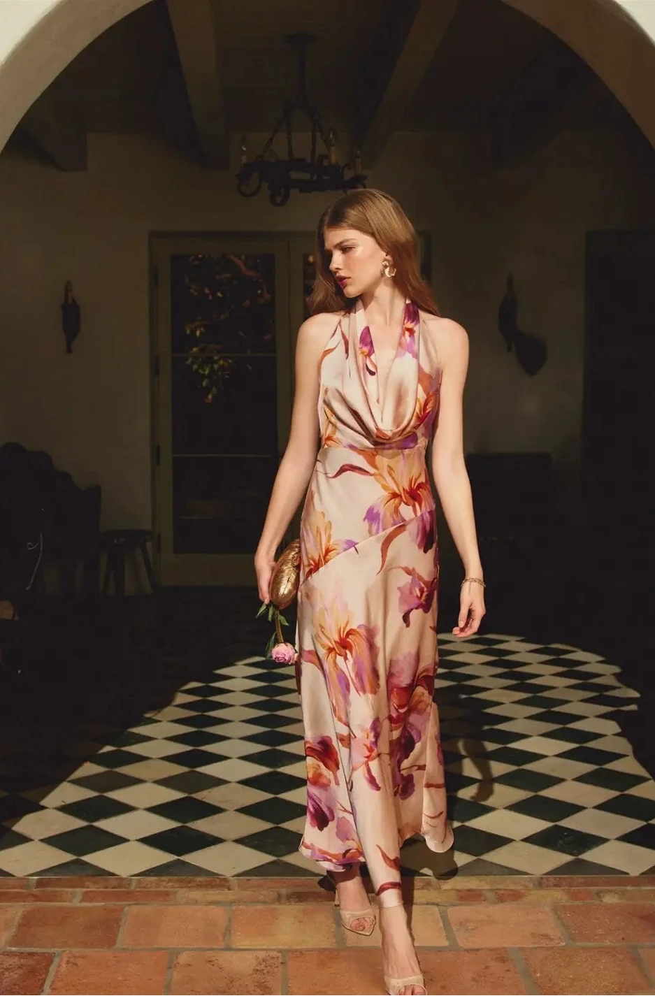 Woman in a floral dress walking through a dimly lit room with checkered floor.