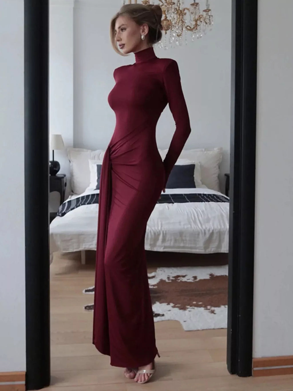 Woman in a burgundy evening gown standing in front of a mirror in a bedroom.