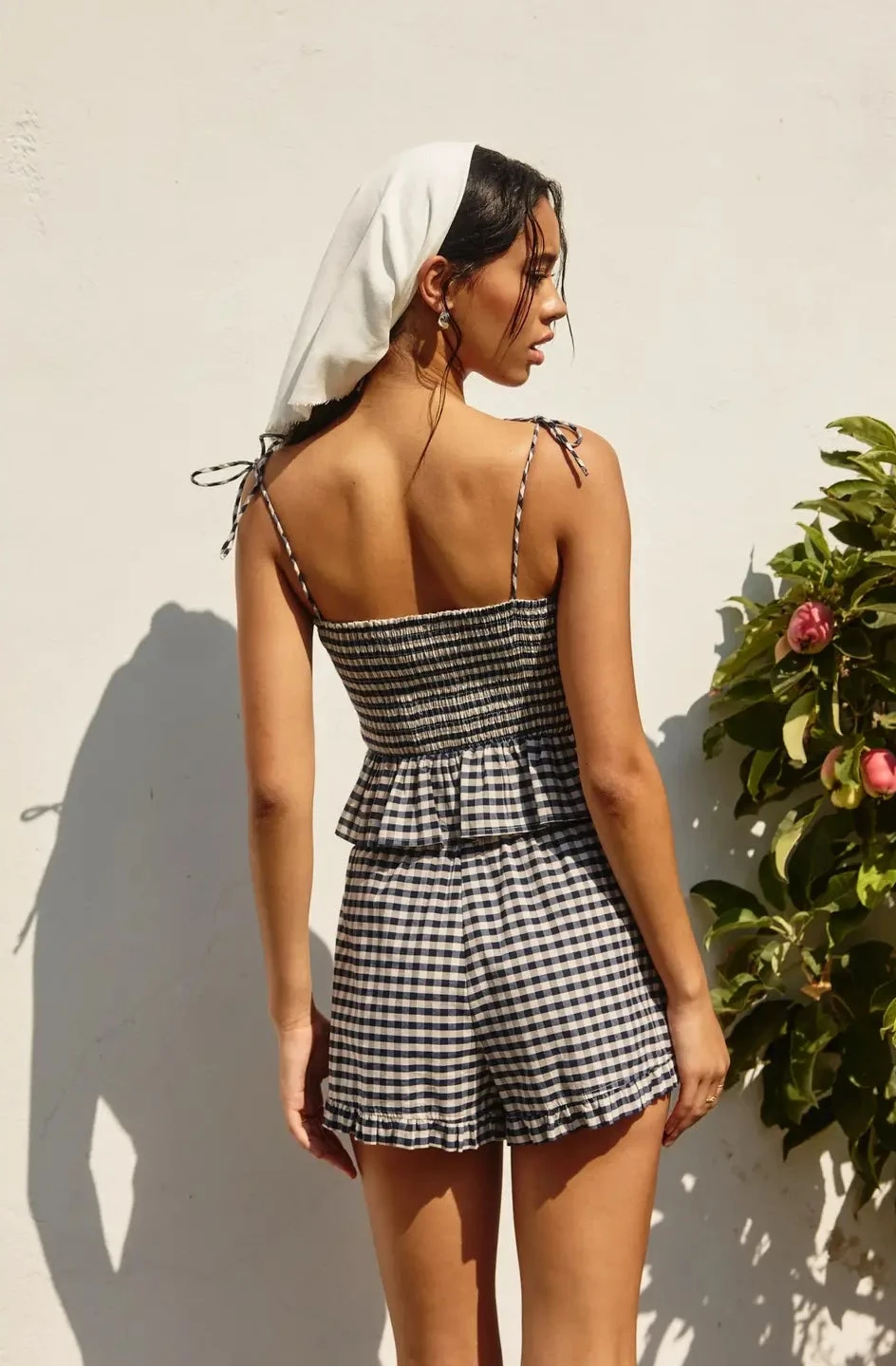 Woman wearing a black and white checkered dress against a light wall with a plant.