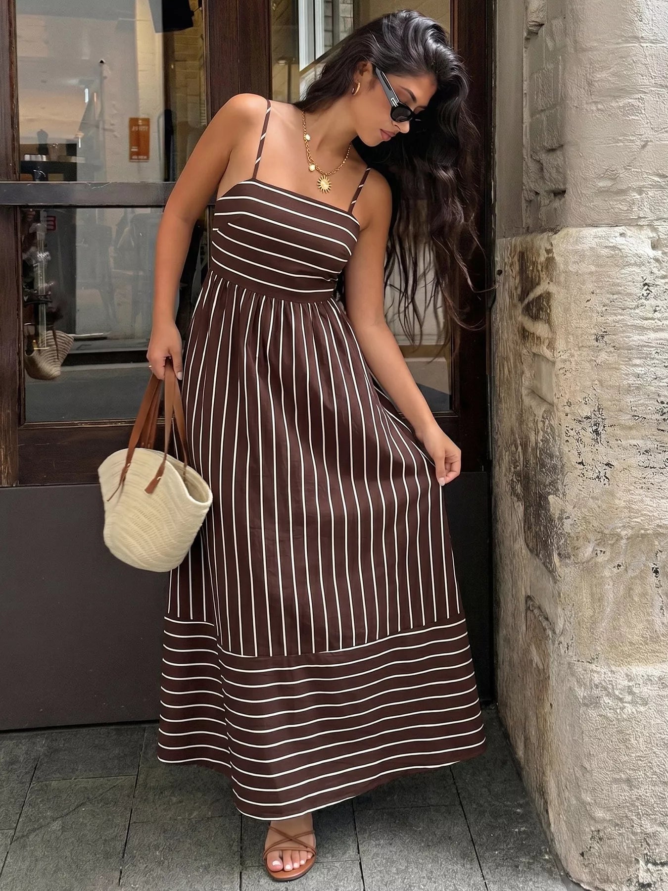 Woman in a brown and white striped dress standing against a stone wall.