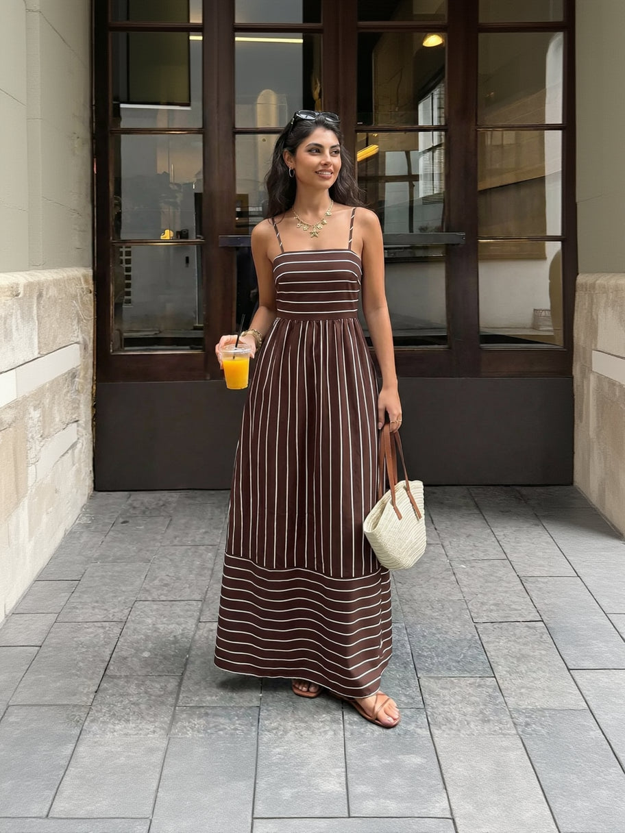 Woman in a brown and white striped dress holding a drink and a bag on a city street.