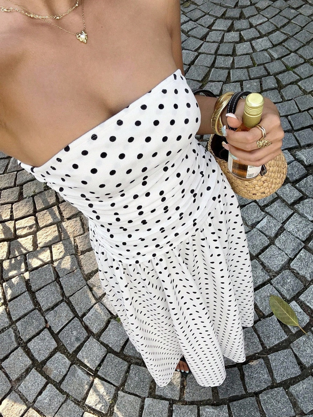 Woman wearing a strapless polka dot dress holding a bottle of wine posing
