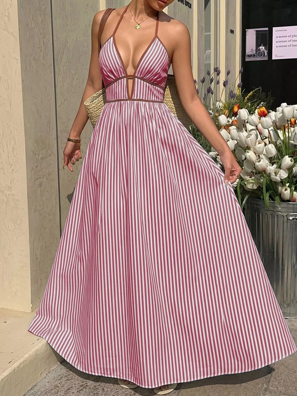 Woman wearing a pink and white striped dress standing outdoors with flowers in the background