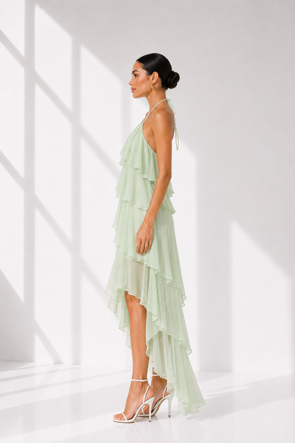 Woman wearing a light green dress with ruffled layers against a white background