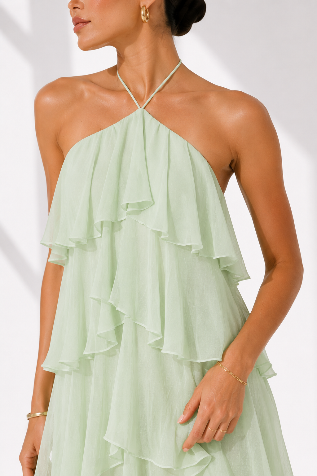 Woman wearing a light green halter neck dress with ruffled layers on a white background