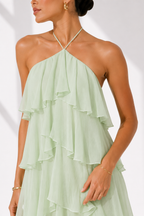 Woman wearing a light green halter neck dress with ruffled layers on a white background
