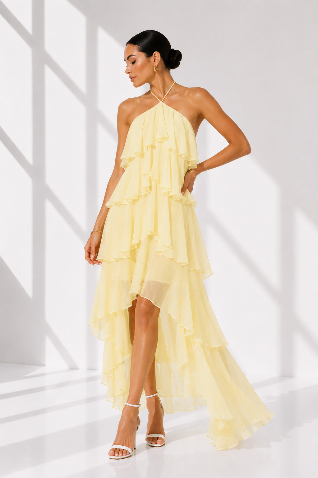 Woman wearing a light yellow halter neck dress with ruffled layers on a white background