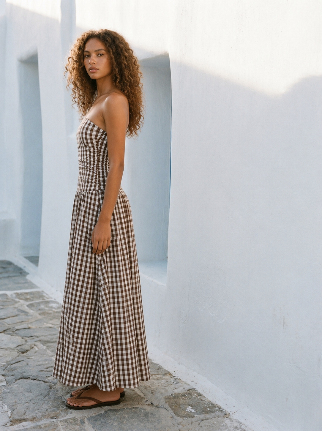 Woman in a checkered dress standing against a white wall.