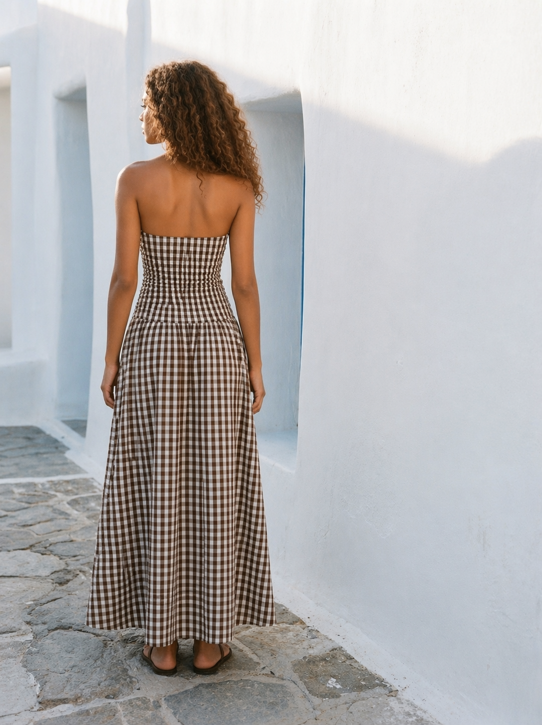 Woman in a strapless checkered dress standing on a stone path with white walls.