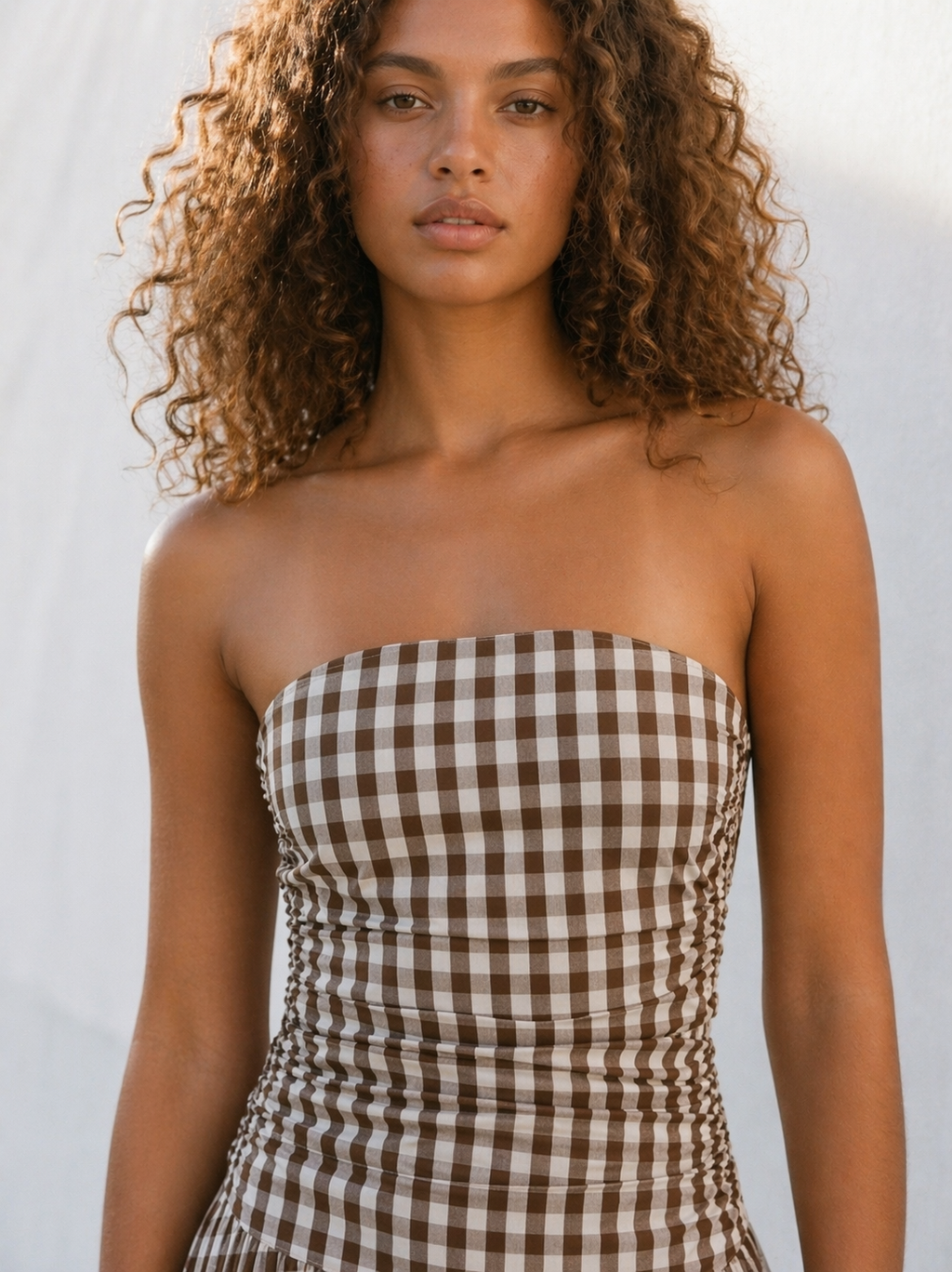 Woman wearing a strapless brown and white checkered dress against a white background