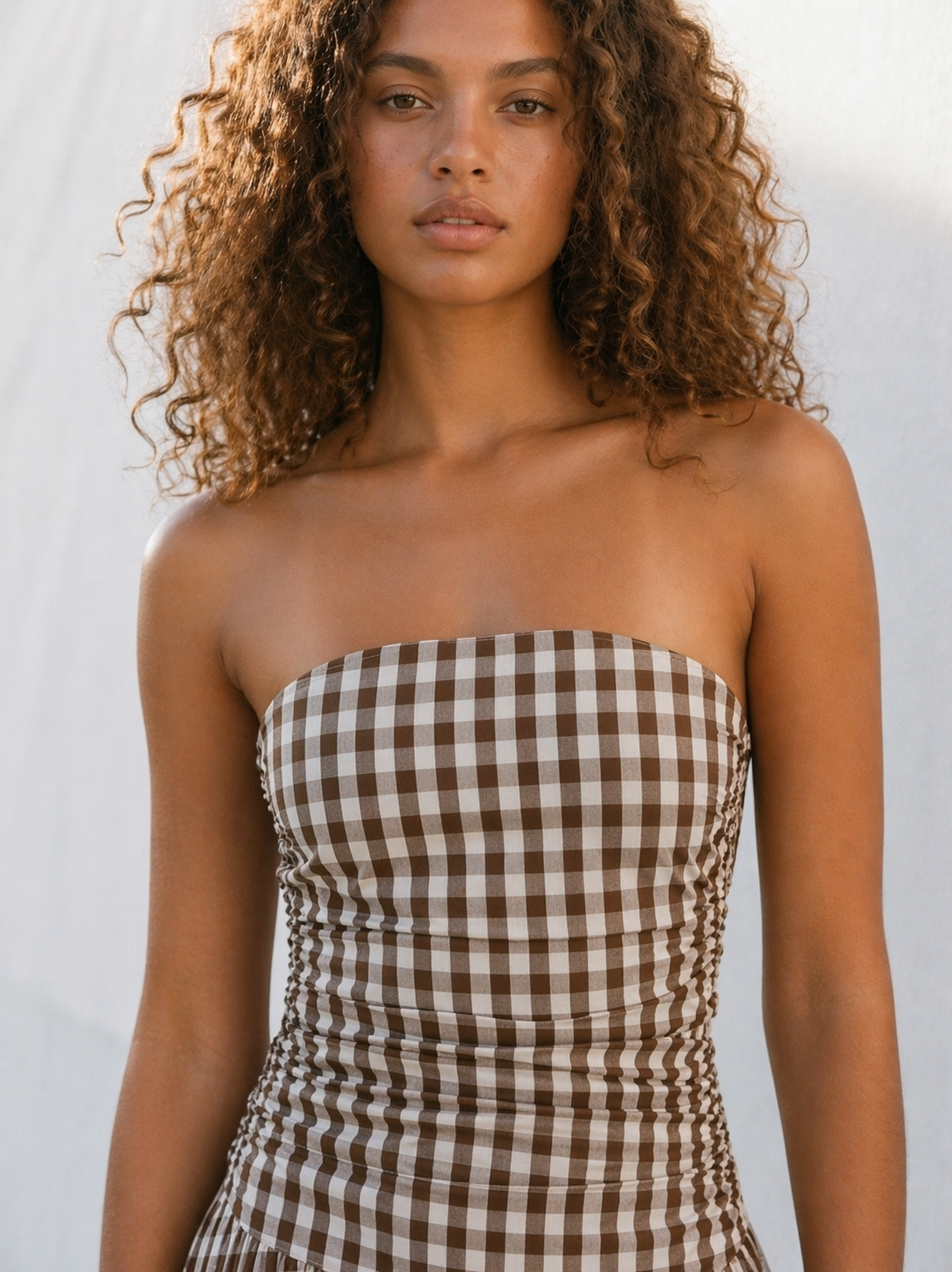 Woman wearing a strapless brown and white checkered dress against a white background