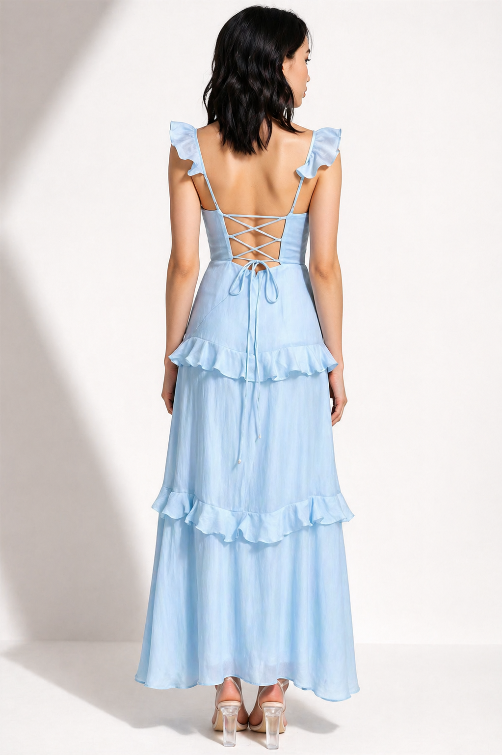 Woman wearing a light blue dress with ruffled layers and lace-up back on a white background