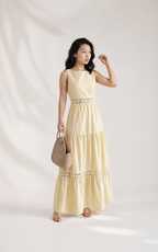 Woman wearing a light yellow dress with lace details, holding a beige handbag on a white background