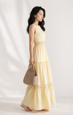Woman wearing a light yellow dress with a textured handbag on a white background
