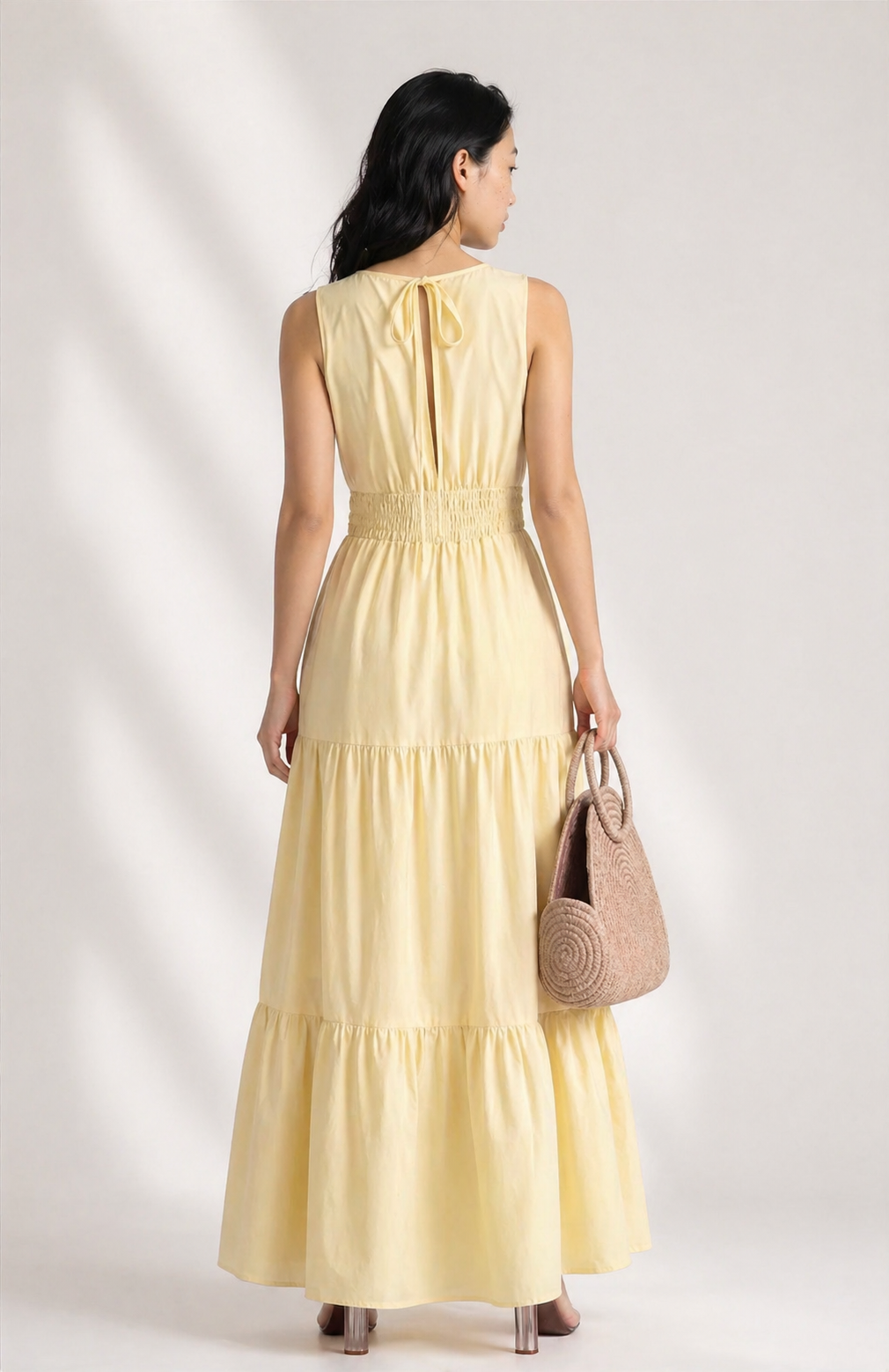 Woman wearing a yellow dress holding a woven bag on a plain background
