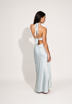 Woman wearing a light blue evening gown with a halter neck and tie details on a white background