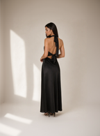 Woman wearing a black evening gown with a deep neckline and long train on a plain background