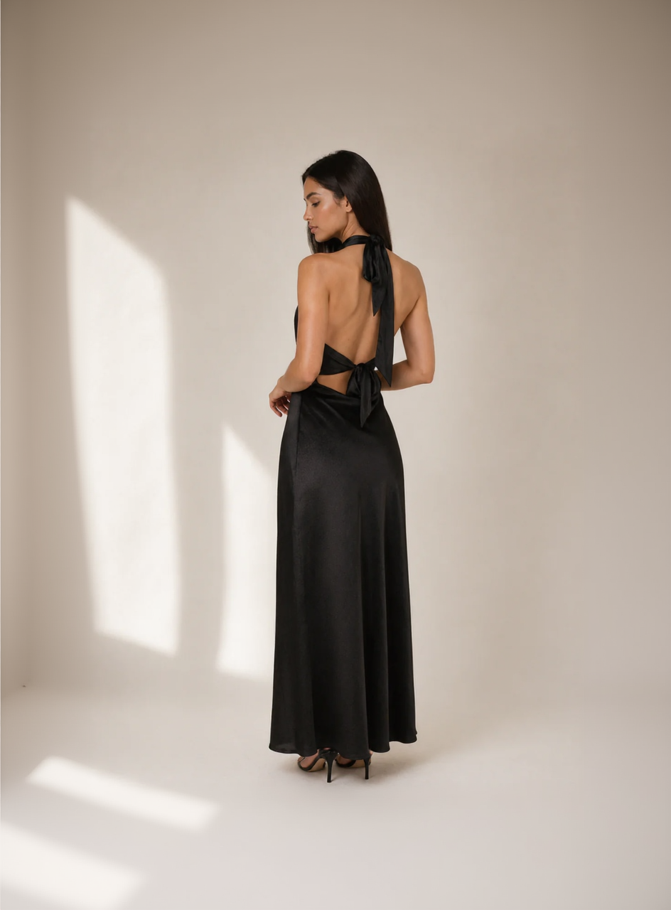 Woman wearing a black evening gown with a deep neckline and long train on a plain background