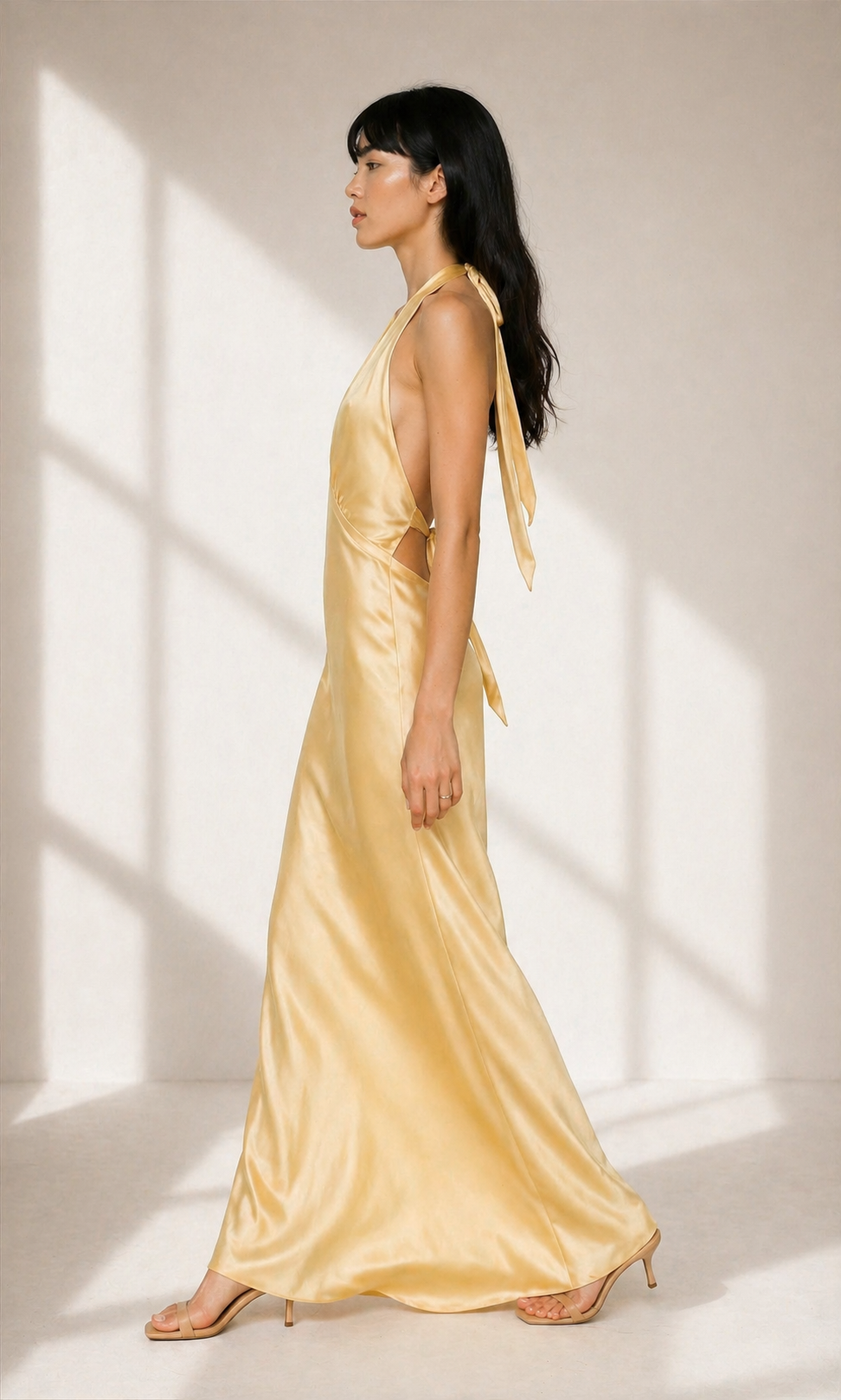 Woman wearing a gold satin dress standing in a softly lit room.
