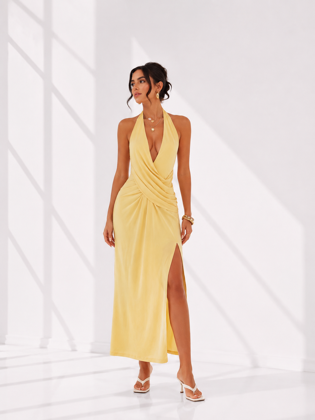 Woman wearing a yellow halter neck dress with a slit on a white background