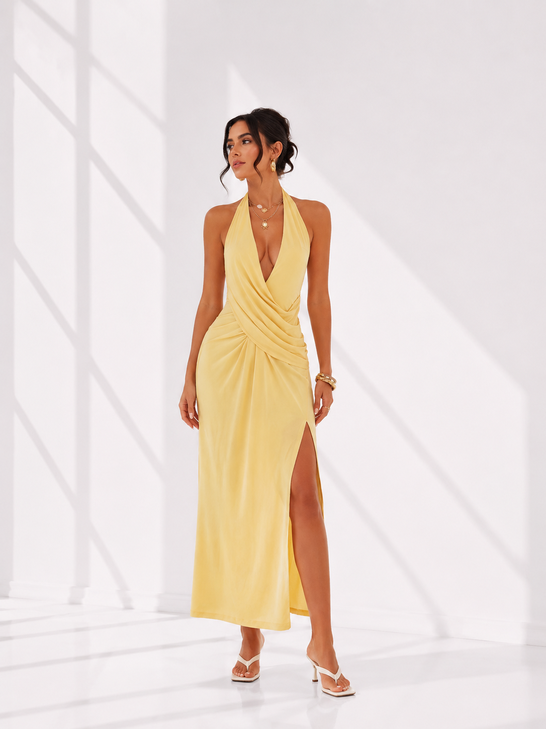 Woman wearing a yellow halter neck dress with a slit on a white background
