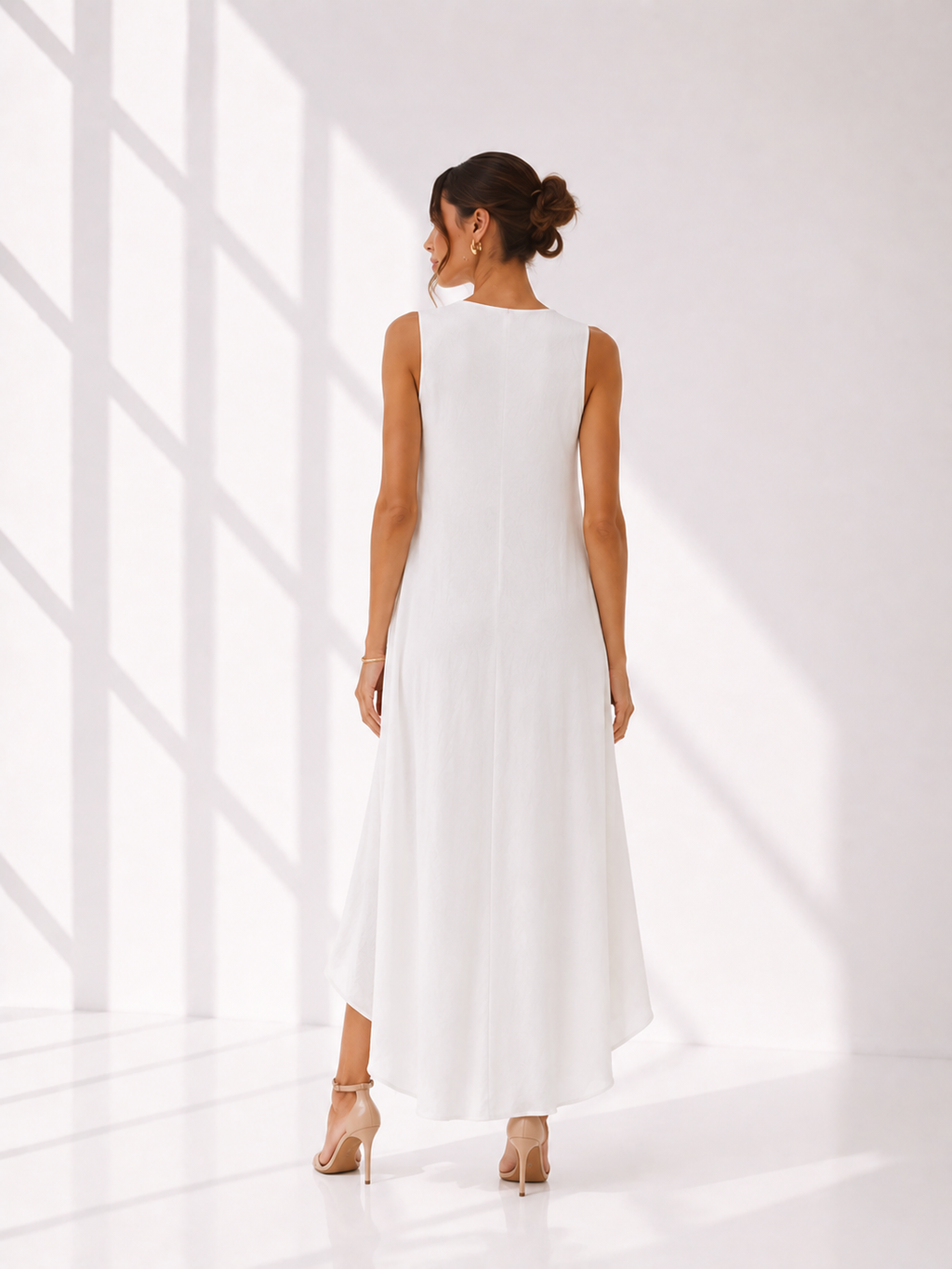 Woman wearing a white sleeveless dress standing in a bright room with sunlight filtering through.