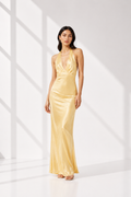 Woman wearing a gold evening gown in a white room with sunlight filtering through.