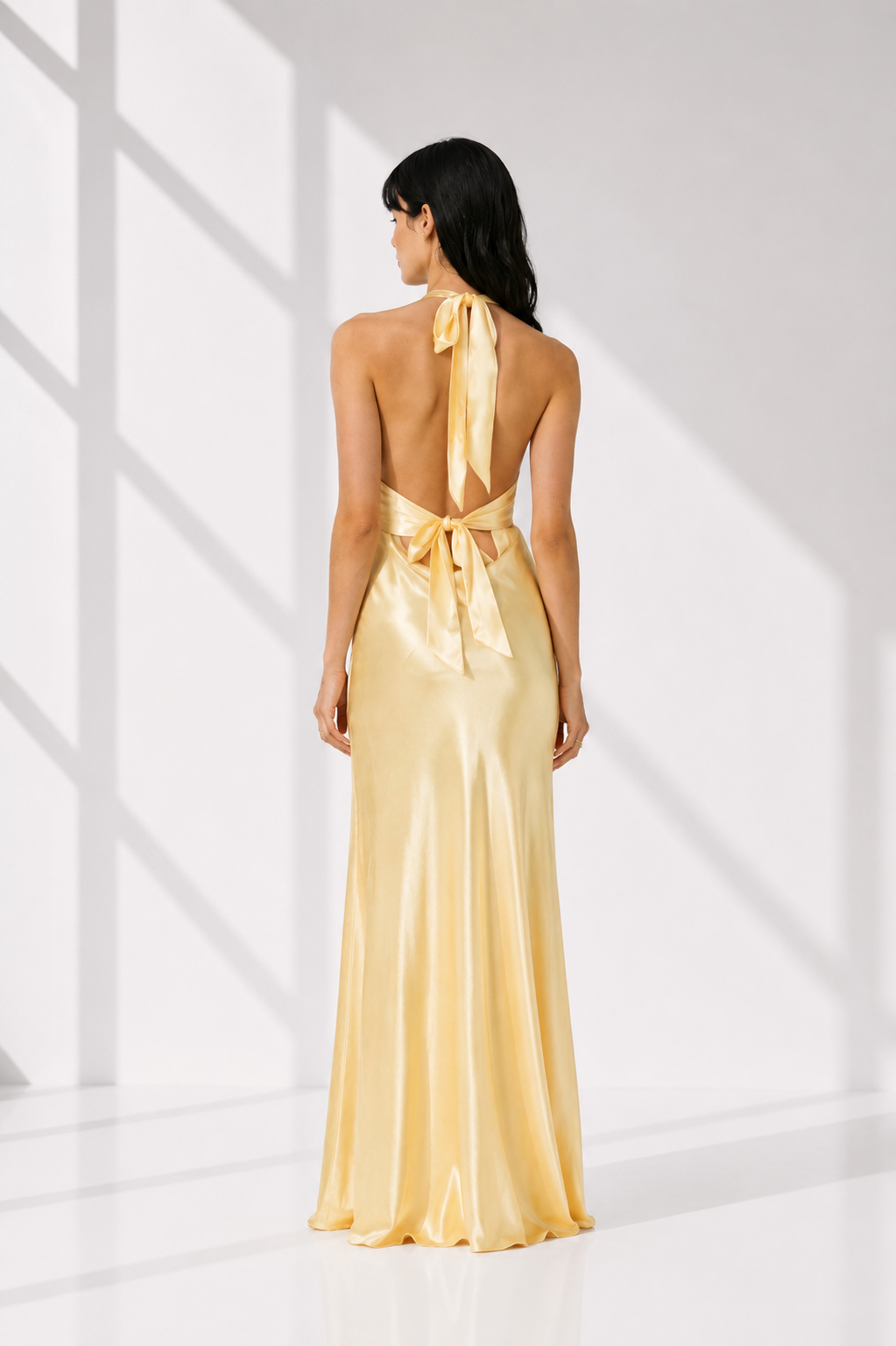 Woman wearing a gold evening gown with a halter neck design in a bright setting