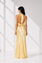 Woman wearing a gold evening gown with a halter neck design in a bright setting