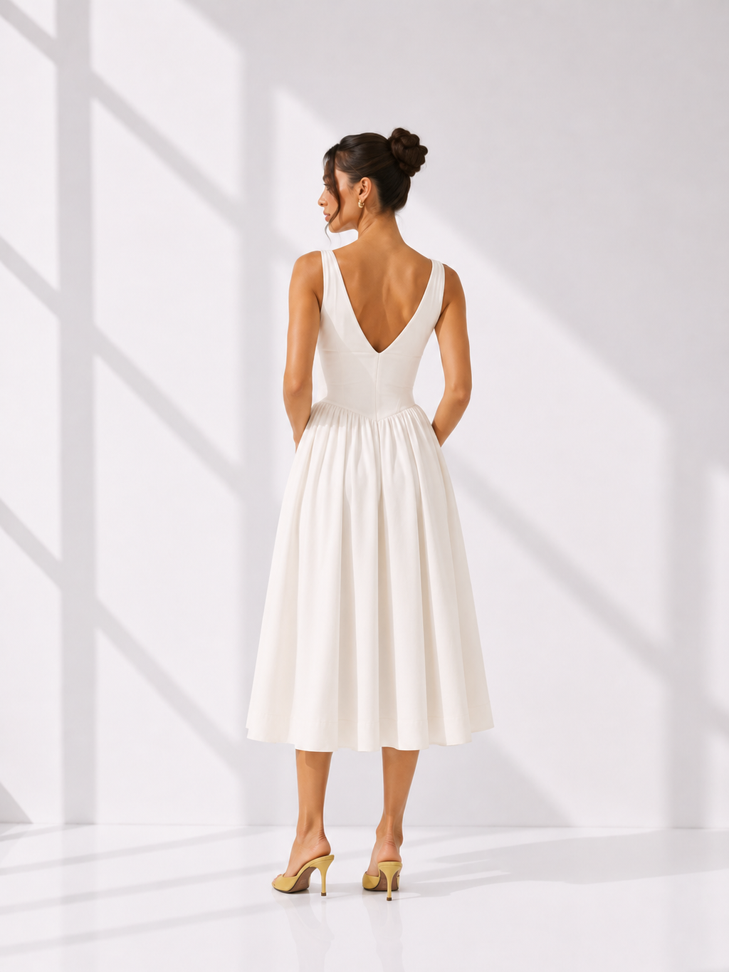 Woman wearing a white dress with a deep neckline and open back, standing in a bright room.