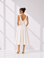 Woman wearing a white dress with a deep neckline and open back, standing in a bright room.
