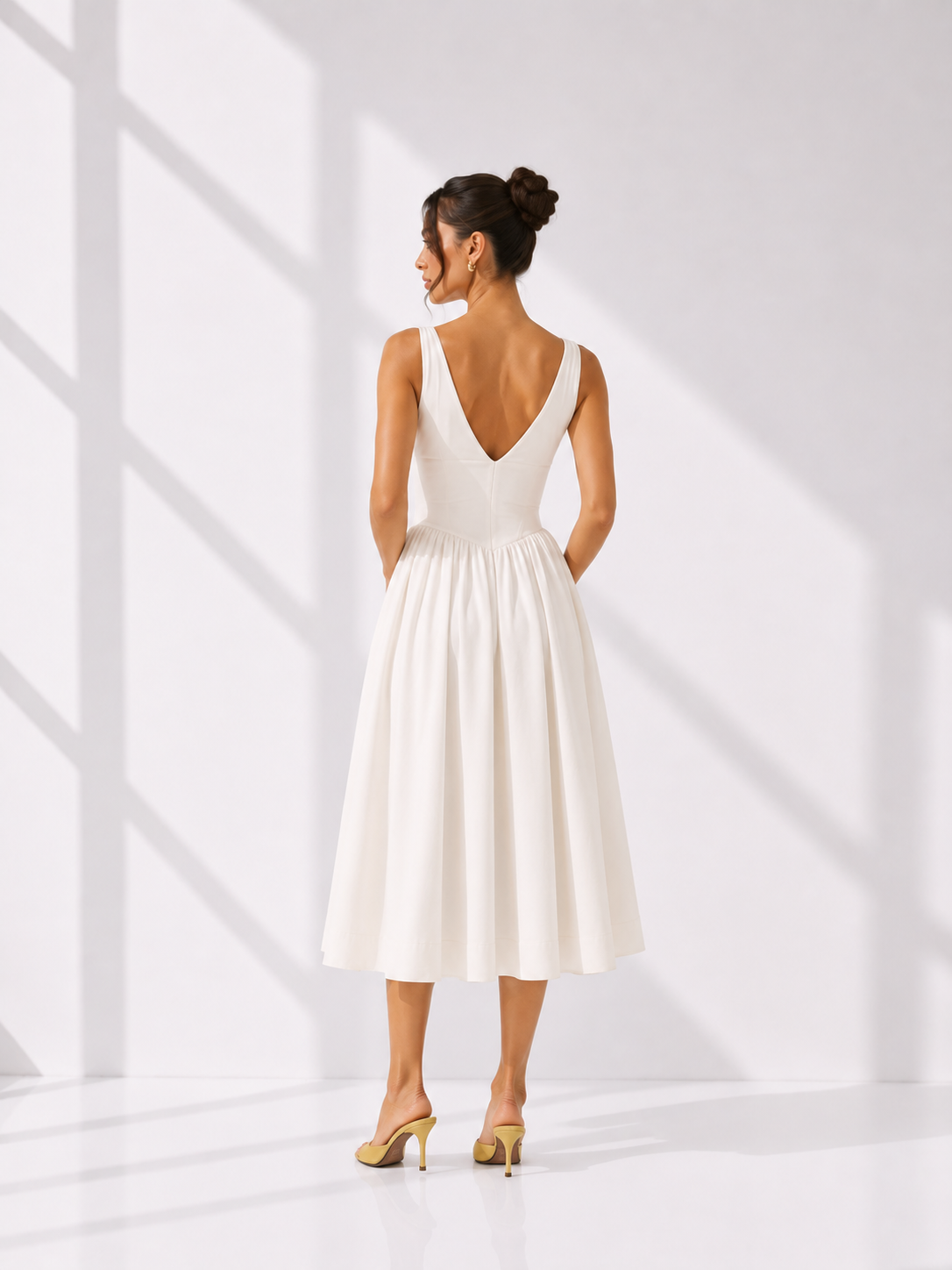 Woman wearing a white dress with a deep neckline and open back, standing in a bright room.