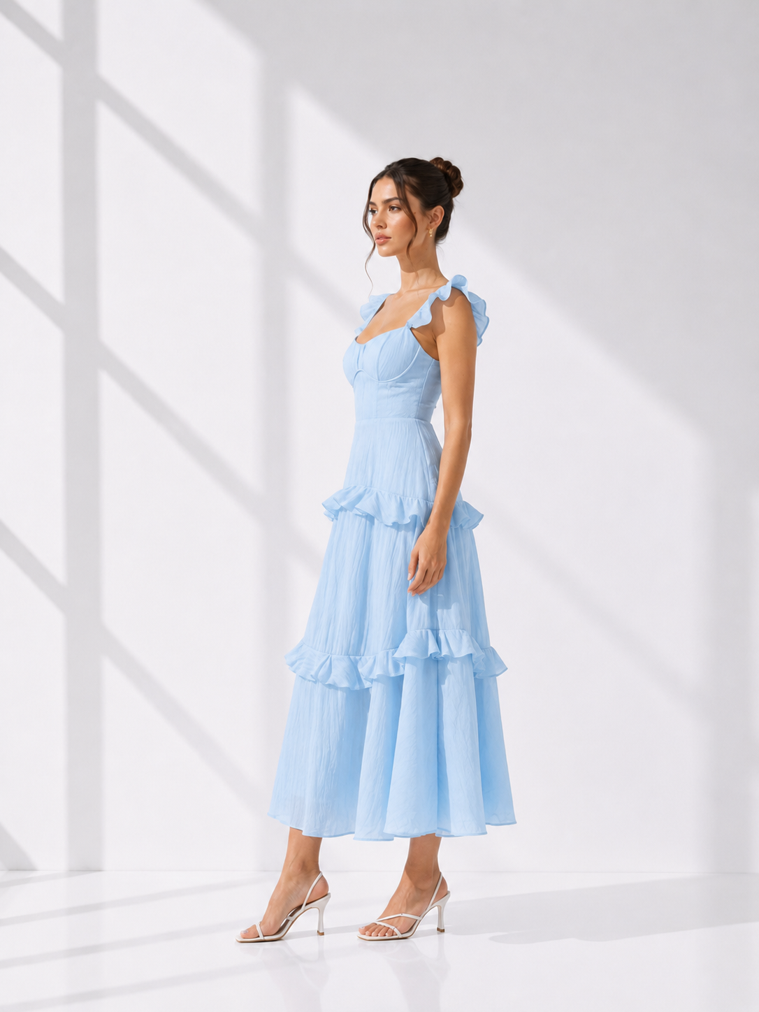 Woman wearing a light blue dress with ruffled layers in a bright room.