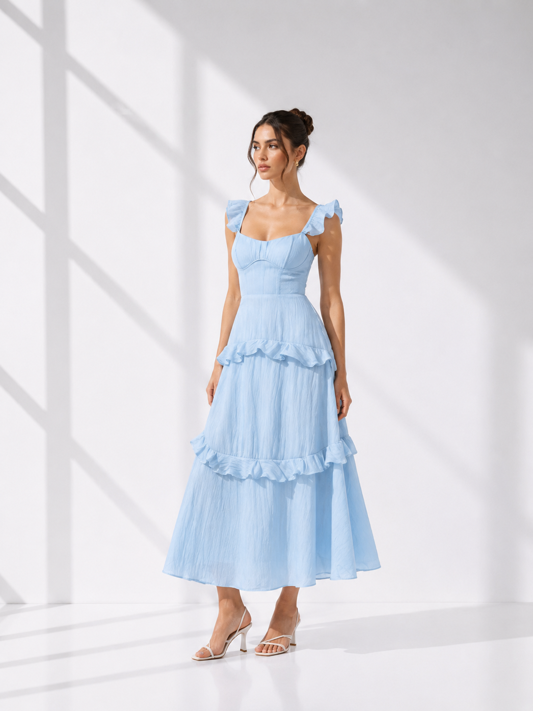 Woman wearing a light blue dress with ruffled layers in a bright room.