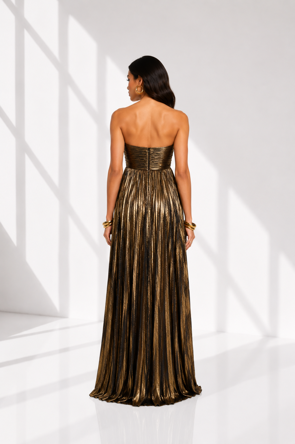Woman wearing a long, strapless gold dress in a bright white room.