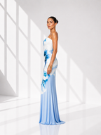 Woman wearing a blue and white floral one-shoulder dress in a bright room.