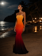 Woman in a strapless gown with gradient color effect standing on a beach at night.