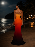 Woman in a strapless red evening gown standing on a beach at night.