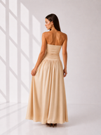 Woman wearing a beige strapless gown standing in a softly lit room.