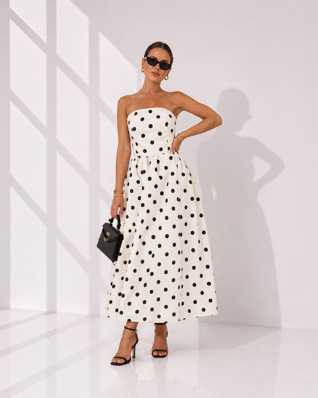 Woman wearing a strapless polka dot dress in a minimal white room.