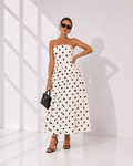 Woman wearing a strapless polka dot dress in a minimal white room.