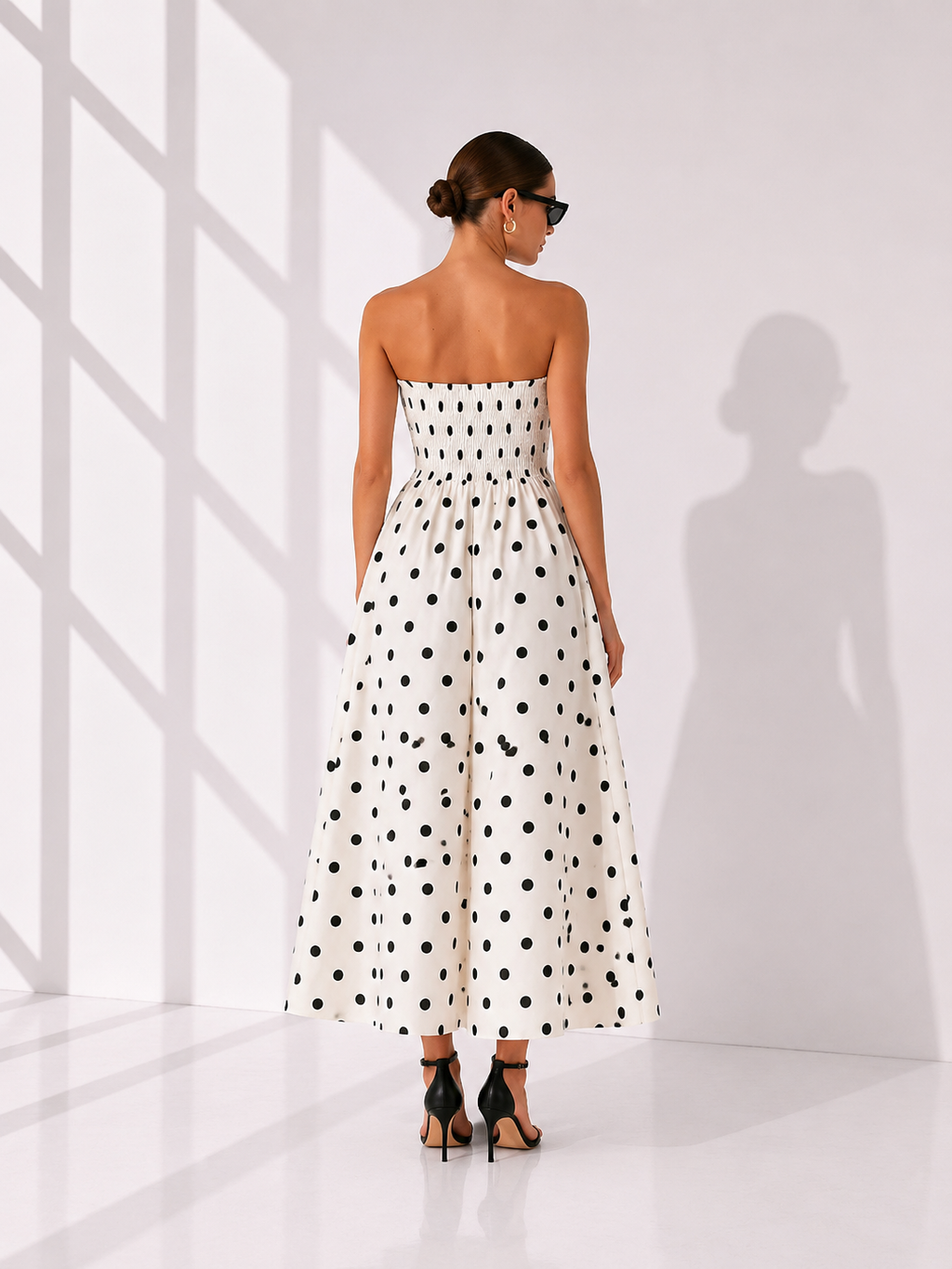 Woman wearing a strapless polka dot dress in a minimal white room.